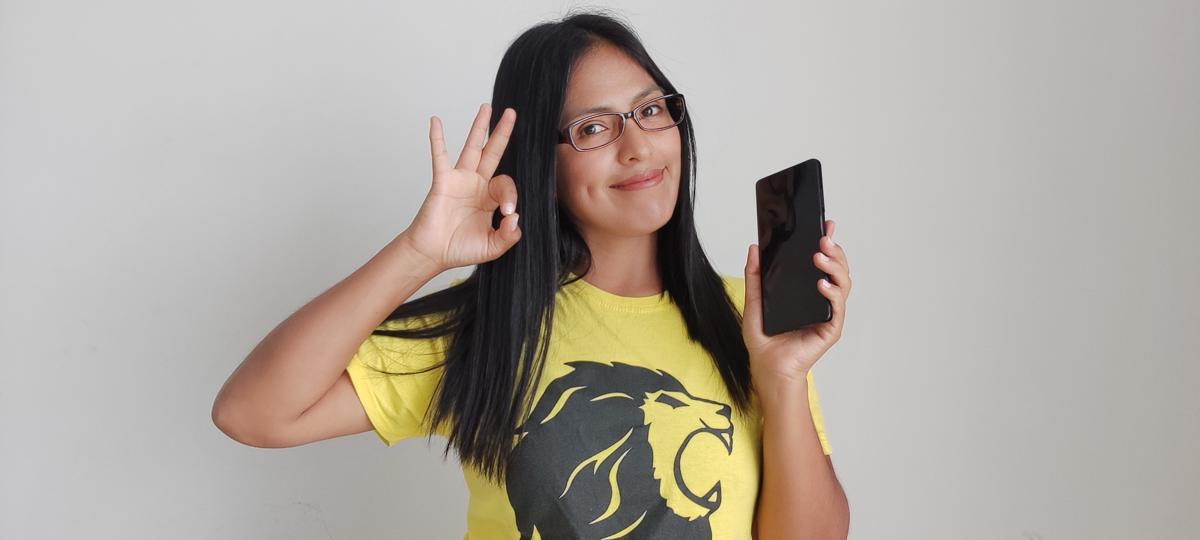 Woman with a yellow shirt with a lion logo, holding her phone in one hand, smiling